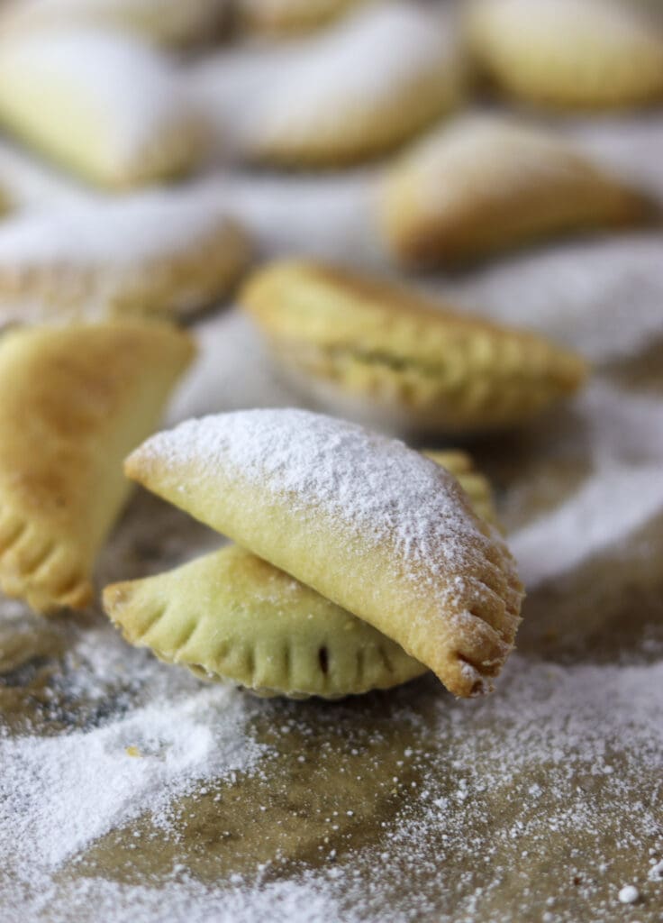 Golden baked and crispy empanada cookie stacked on top of another cookie with more cookie empanadas in the background